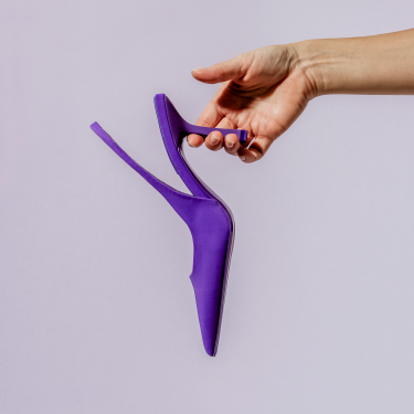Purple high heeled shoe being held in front of a lavender background